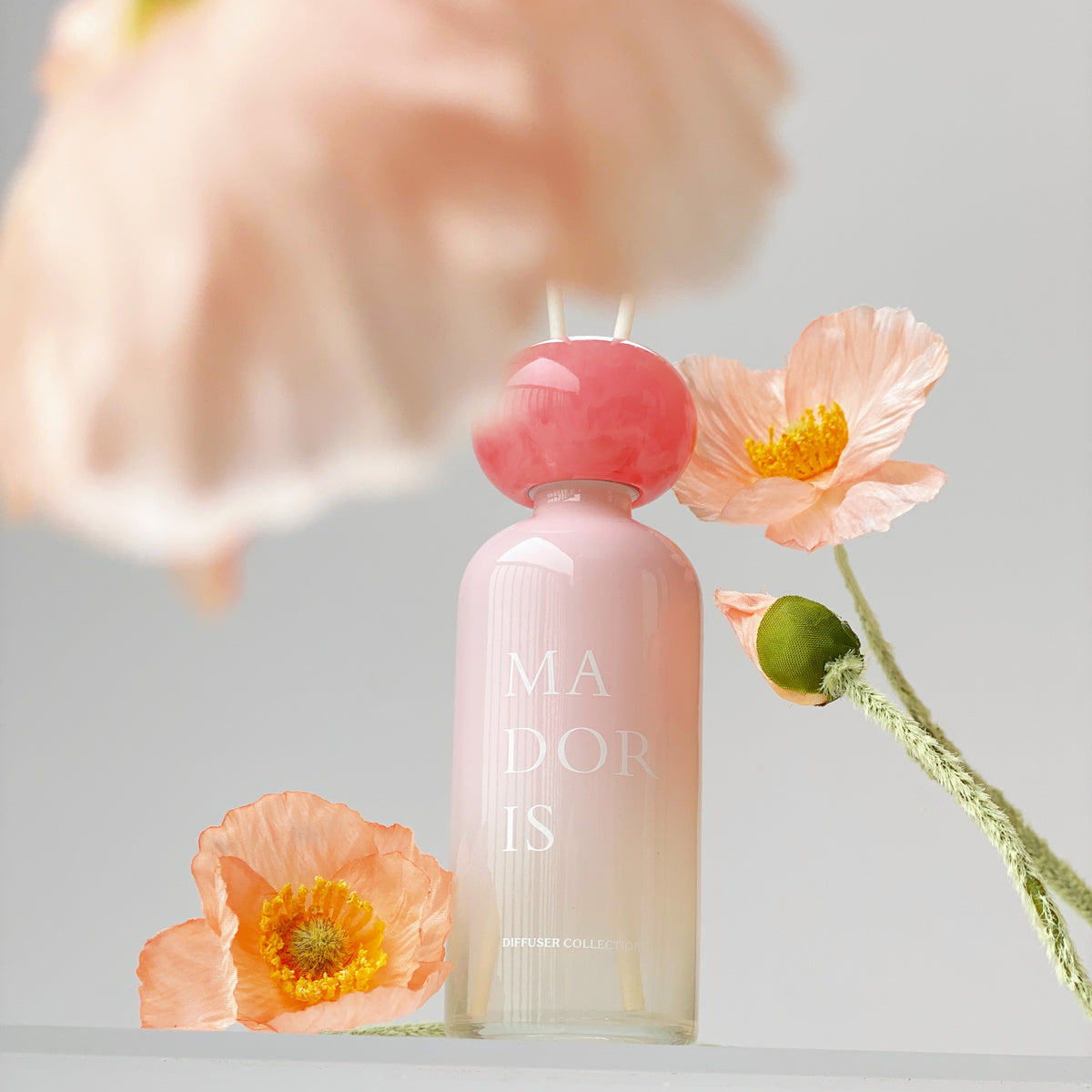 MADORIS Blush Veil reed diffuser displayed with delicate flowers in a soft pink setting