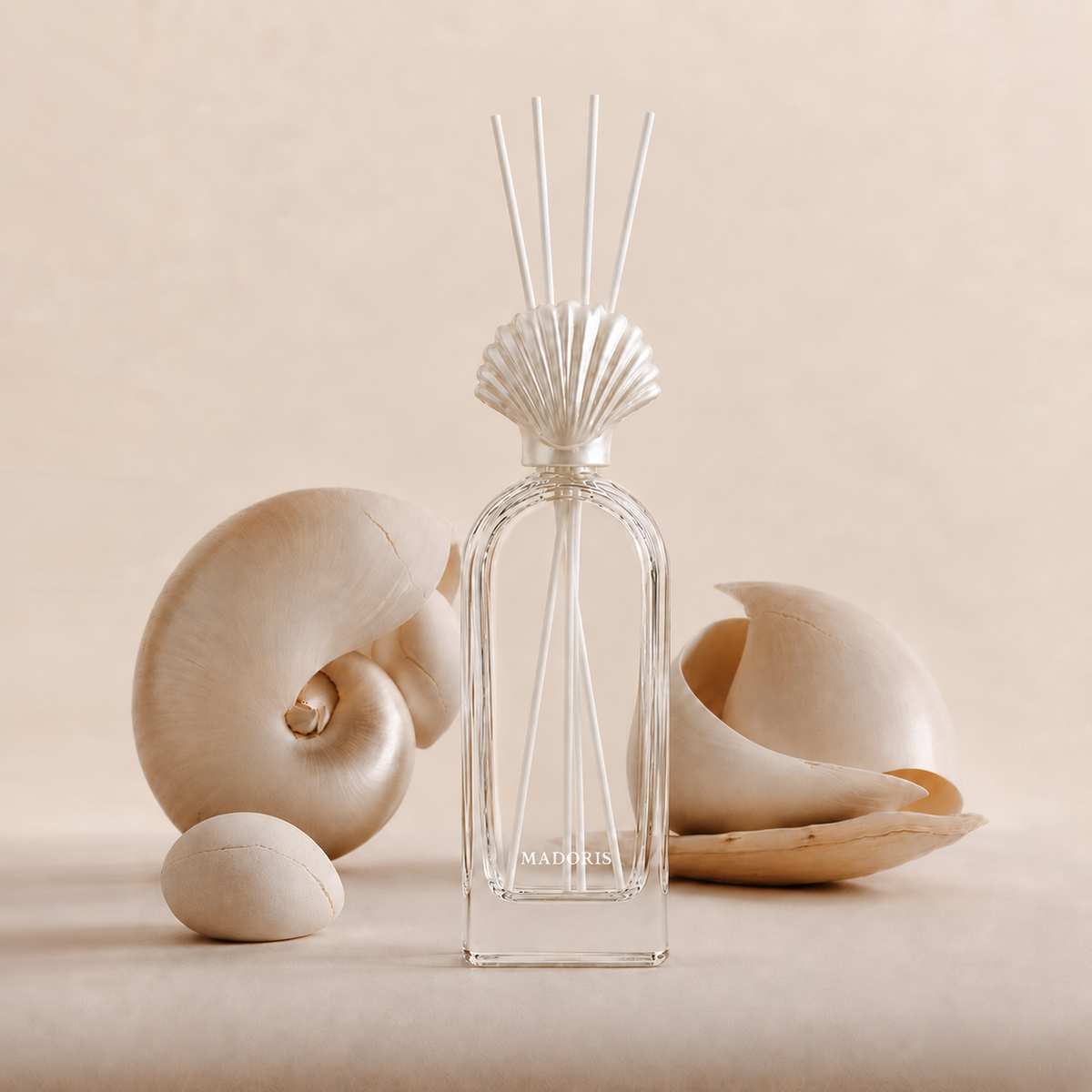 MADORIS Cashmere Amber reed diffuser with pearl-white shell cap styled with sculptural seashell forms on a warm beige background