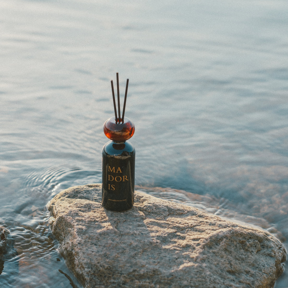 MADORIS Moonlight Glass reed diffuser displayed on rocks beside the sea
