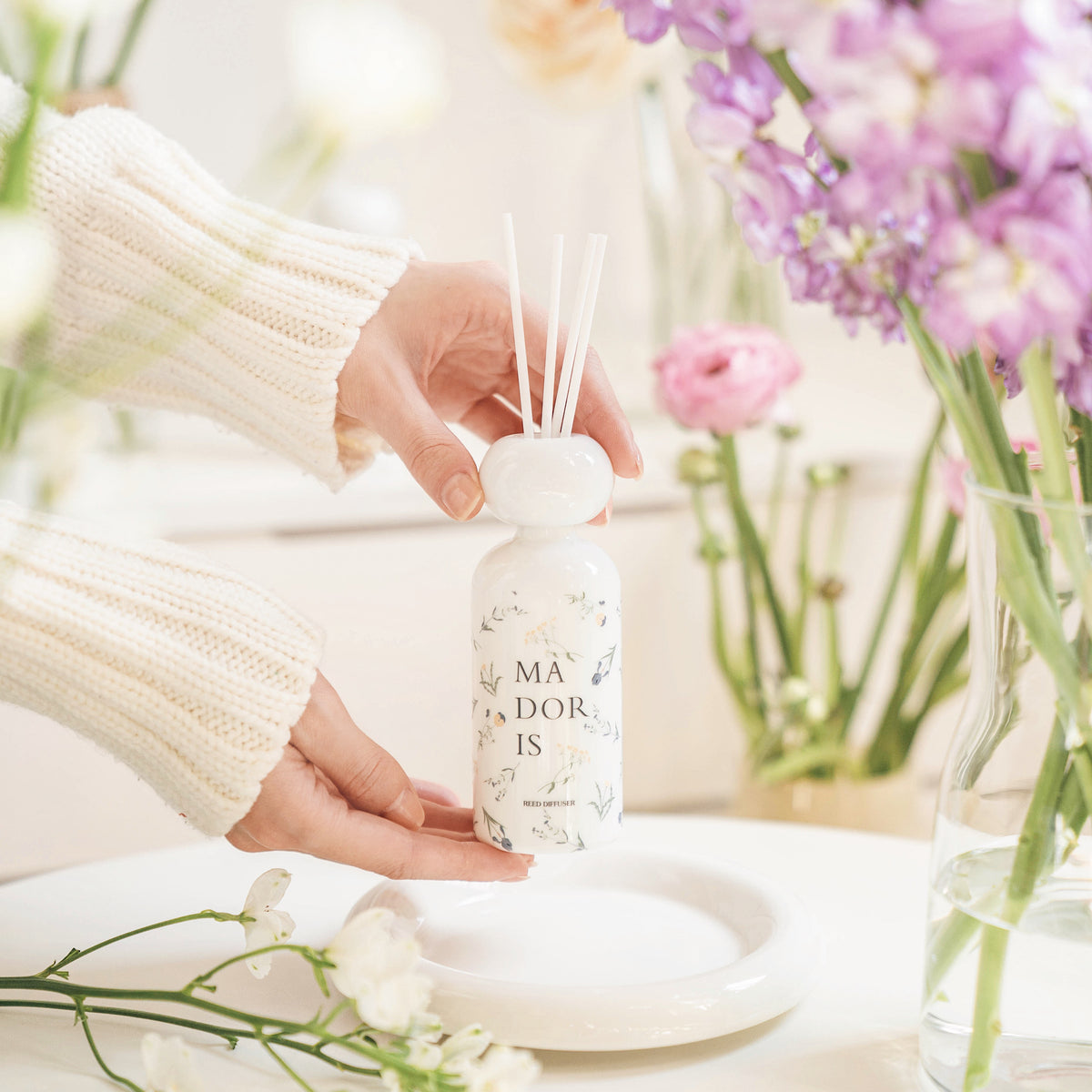 MADORIS White Whisper reed diffuser styled with pale flowers in a soft elegant setting